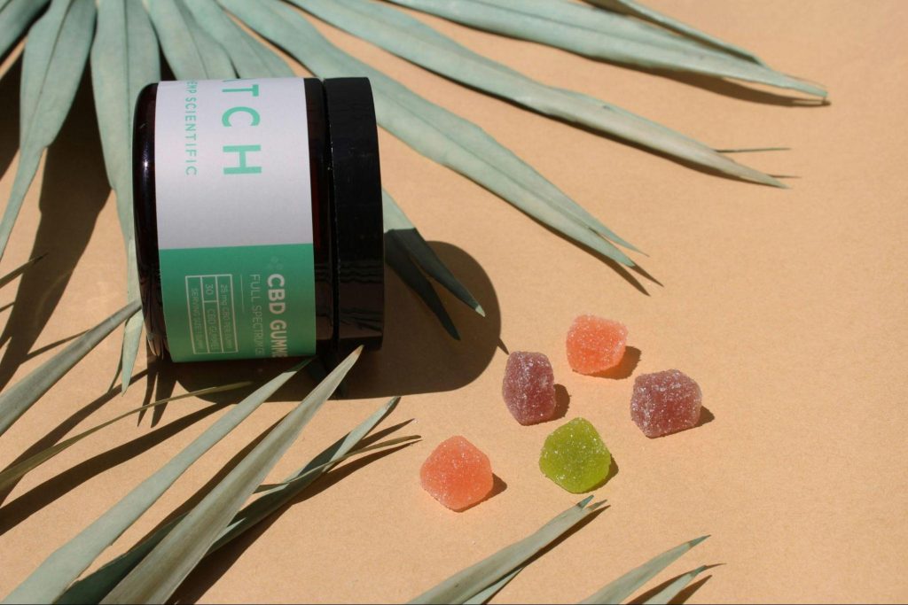 Jar of CBD gummies with colorful pieces arranged on a neutral background, reflecting how alternative wellness products are styled and shared online