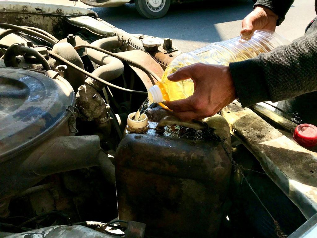 Mechanic pouring engine coolant into a car radiator as part of routine preventive vehicle maintenance to extend engine life and reduce repair costs
