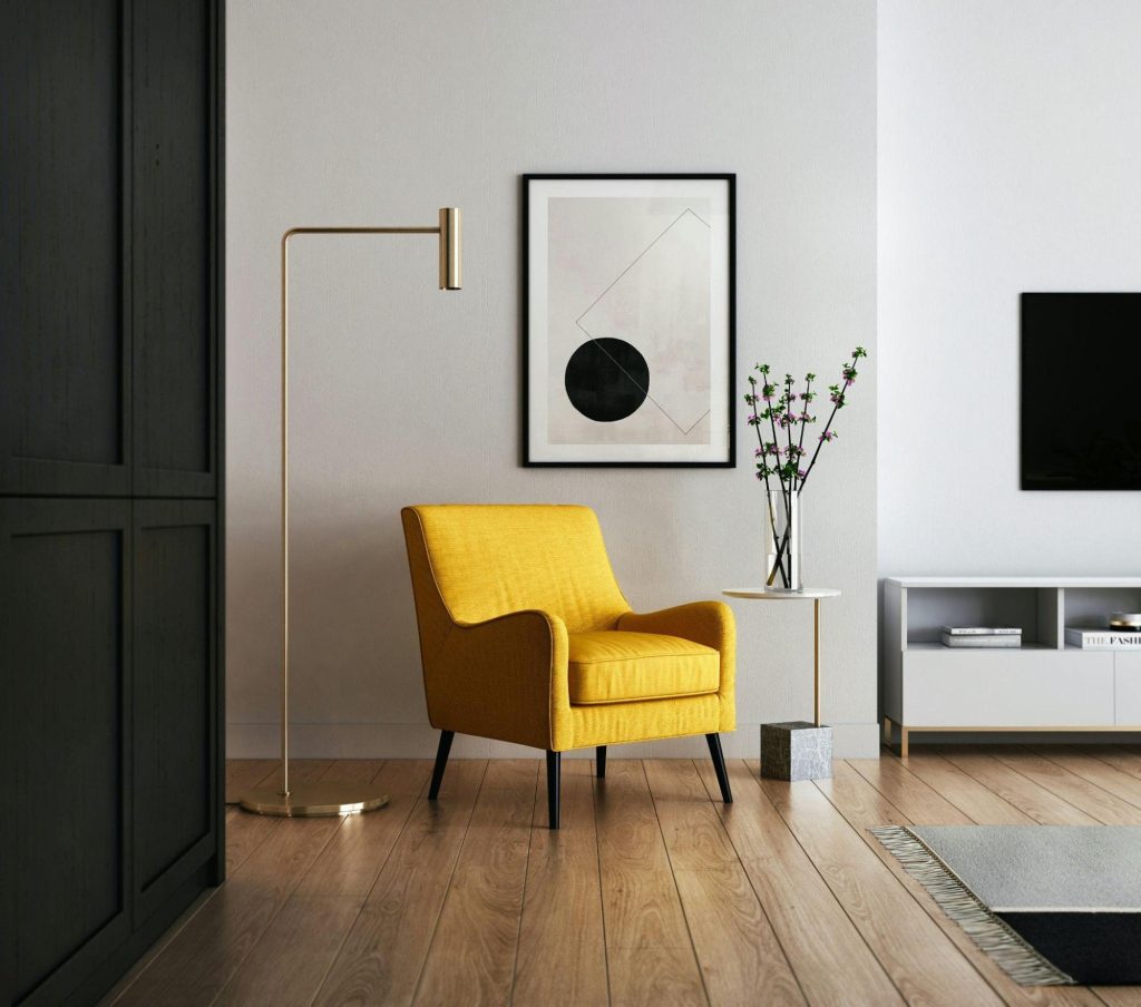 Yellow accent chair in a minimalist living room with neutral walls, modern floor lamp, framed art, and light wood flooring